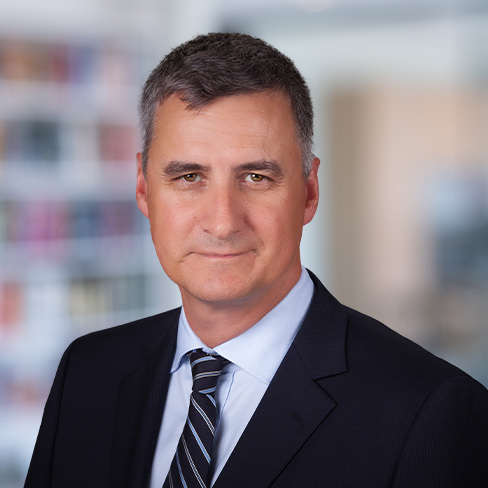 A middle-aged man in a dark suit and striped tie poses for a professional headshot with a blurred corporate law office background, reflecting the professionalism of top lawyers in Chicago.