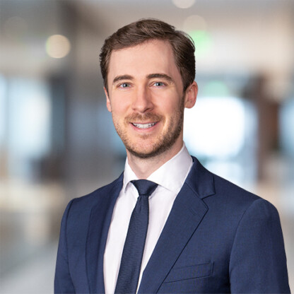 A man in a navy blue suit and tie stands smiling in an office with a blurred background, representing Chicago lawyers specializing in intellectual property law.