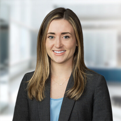 A woman with straight, light brown hair wearing a gray blazer and a blue top, smiling in a modern, blurred office setting—reflecting the professionalism of lawyers in Chicago.