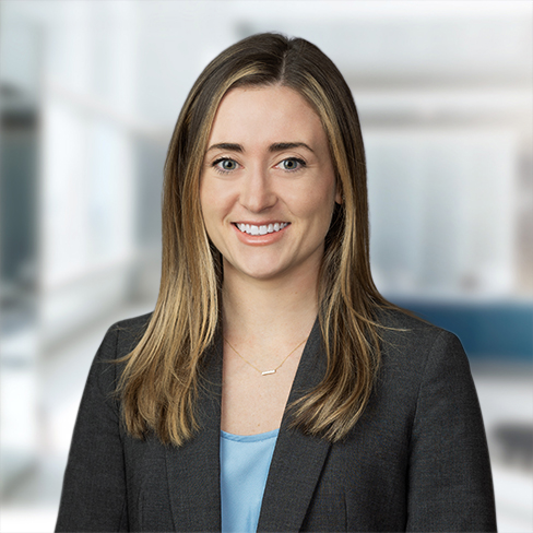 A woman with straight, light brown hair wearing a gray blazer and a blue top, smiling in a modern, blurred office setting—reflecting the professionalism of lawyers in Chicago.