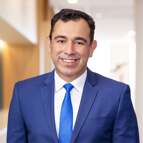A man in a blue suit and tie smiles at the camera in a bright, modern corporate law office, reflecting the professional atmosphere of leading law offices.