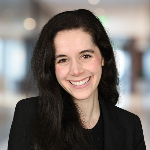 Woman with long dark hair, wearing a black blazer and black top, smiling at the camera in a blurred corporate law office, representing Chicago lawyers.