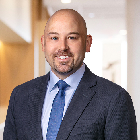 A man in a dark suit, light blue shirt, and blue tie smiles at the camera in a modern, well-lit corporate law office—a setting familiar to many Chicago lawyers.