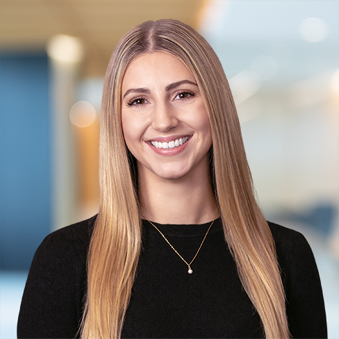 A woman with long, straight blonde hair wearing a black top and gold necklace smiles in a modern corporate law office alongside top lawyers in Chicago.
