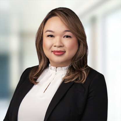 A woman with shoulder-length brown hair wearing a black blazer and white blouse stands in a bright, blurred office setting, representing litigation support at leading law offices.