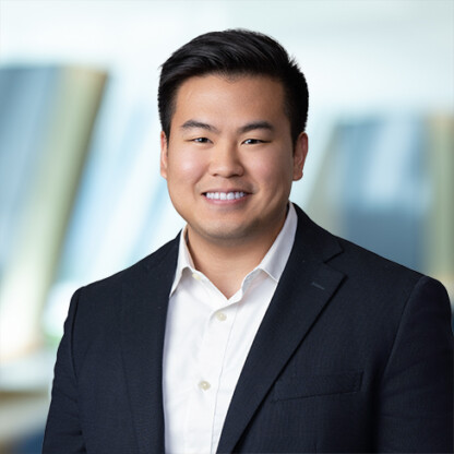 A man in a dark suit jacket and white shirt smiles at the camera with a blurred corporate law office background, reflecting the professionalism of top Chicago lawyers.