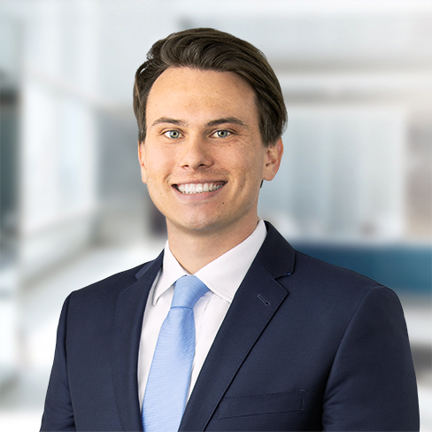A man in a navy suit and light blue tie smiles at the camera, standing in a bright, modern office setting typical of top law offices for chicago lawyers.