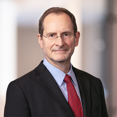 A middle-aged man in a suit, light blue shirt, and red tie, wearing glasses, stands against a softly blurred indoor background—reflecting the professionalism found in top lawyers in Chicago.