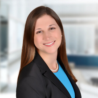 Woman with straight brown hair wearing a black blazer, blue top, and pearl necklace, smiling in a bright, modern office—an experienced professional offering litigation support for lawyers in Chicago.