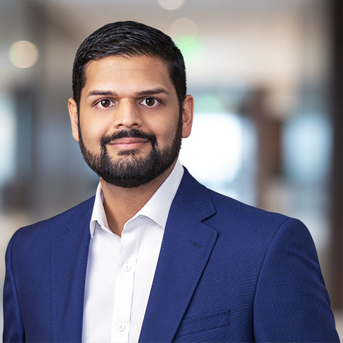 A man with short dark hair and a beard, wearing a blue suit jacket and white shirt, stands in a blurred corporate law office, reflecting the professional environment of Chicago lawyers.