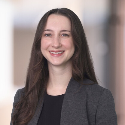 A woman with long brown hair, wearing a dark blazer over a black top, smiles at the camera against a blurred indoor background, reflecting the professionalism often seen in law offices and among lawyers in Chicago.