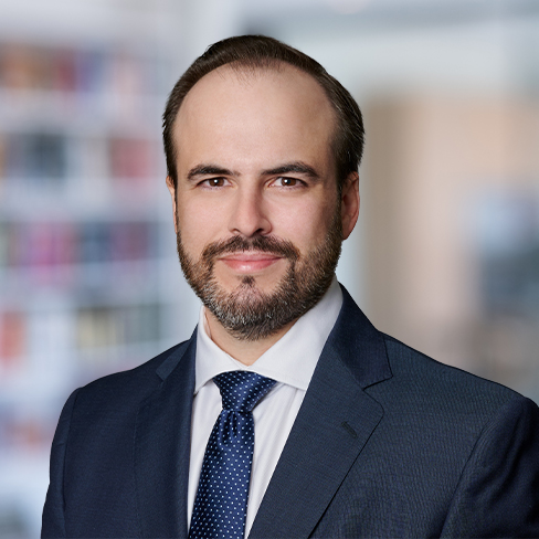 A man in a navy suit, white shirt, and dotted tie poses in front of a blurred corporate law office, embodying the professionalism of top lawyers in Chicago.