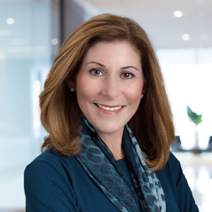 A woman with shoulder-length brown hair, wearing a blue top and patterned scarf, smiles while standing in a modern law office, reflecting the professional atmosphere of Chicago lawyers.