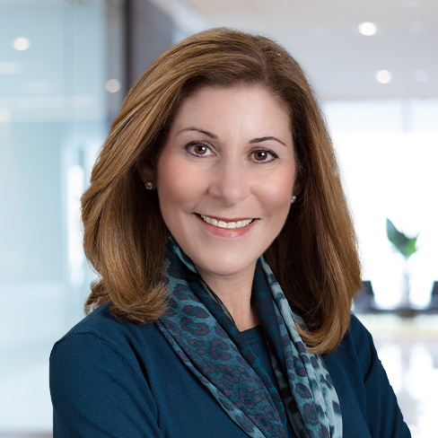 A woman with shoulder-length brown hair, wearing a blue top and patterned scarf, smiles while standing in a modern law office, reflecting the professional atmosphere of Chicago lawyers.