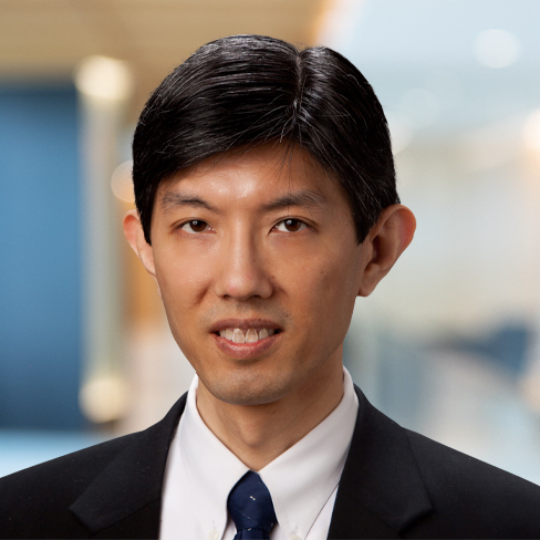 A man with short black hair wearing a dark suit, white shirt, and dark tie, stands in an office setting with a blurred background—typical of professionals in Chicago law offices offering litigation support.