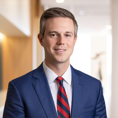 A man in a blue suit, white shirt, and red-striped tie stands indoors in a well-lit hallway, smiling slightly—reflecting the confidence and professionalism of top lawyers in Chicago.