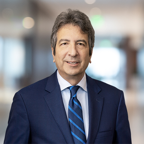 A man in a navy suit and blue striped tie stands indoors with a blurred office background, embodying the professionalism of lawyers in Chicago specializing in intellectual property law.