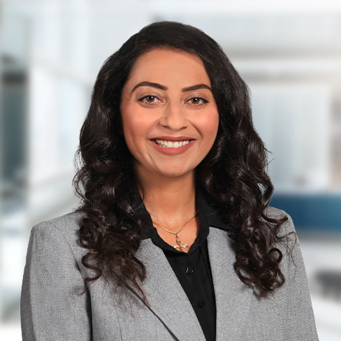 A woman with long, dark, curly hair wearing a gray blazer and black shirt smiles at the camera in a brightly lit corporate law office of Chicago lawyers.