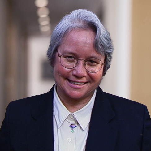 An older person with short gray hair, glasses, and a dark suit smiles while standing in a corridor with blurred lights in the background, reflecting the confidence of seasoned lawyers in Chicago.