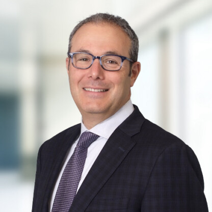 A man in a dark suit, light shirt, and patterned tie smiles at the camera in a bright, modern corporate law office—a fitting setting for chicago lawyers and litigation support professionals.