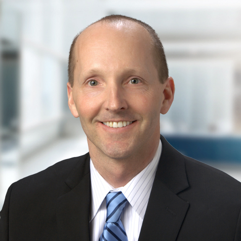 A man in a suit and blue striped tie smiles at the camera with a blurred office background, embodying the professionalism of Chicago lawyers and modern law offices.