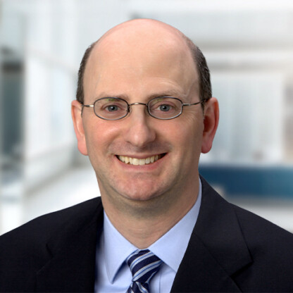 Man with glasses, balding head, and wearing a suit and tie, smiling at the camera in a modern corporate law office, representing top lawyers in Chicago.