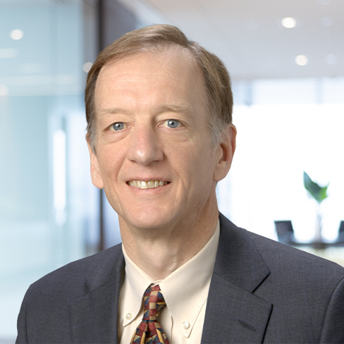 Middle-aged man in a suit and patterned tie smiling in a modern office setting with glass walls, representing lawyers in Chicago who specialize in litigation support.