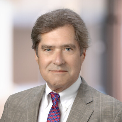 A middle-aged man wearing a gray plaid suit, white shirt, and red patterned tie, poses confidently against a blurred background, embodying the professionalism found in top corporate law office settings.