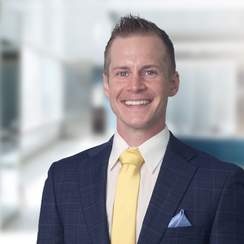 A man in a blue suit, white shirt, and yellow tie stands smiling in a bright, modern corporate law office.