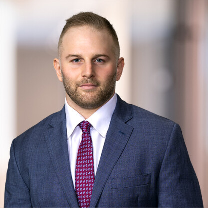 A man in a blue suit, white dress shirt, and patterned red tie stands in front of a blurred corporate law office background, representing Chicago lawyers.