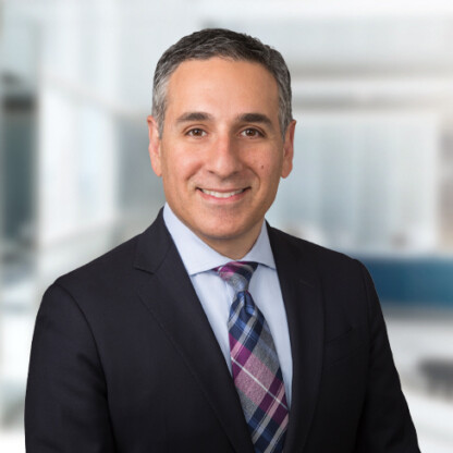A man in a dark suit, light blue shirt, and patterned tie smiles at the camera in a modern corporate law office, reflecting the professionalism of Chicago lawyers.