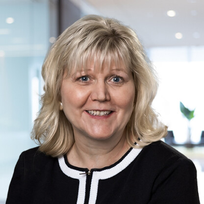 A woman with shoulder-length blonde hair, wearing a black top with white trim, is smiling in a modern law office setting, reflecting the professional environment of Chicago lawyers.