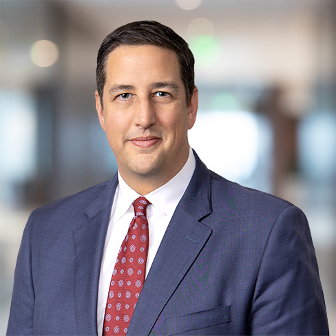 A man in a blue suit, white shirt, and red patterned tie stands in a law office setting, looking at the camera with a neutral expression—reflecting the professionalism of lawyers in Chicago.