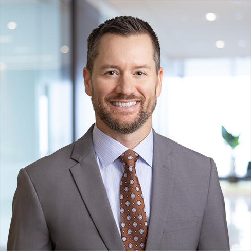 Man in a gray suit and patterned tie smiling, standing in a modern office environment with glass walls—reflecting the professionalism of leading lawyers in Chicago.