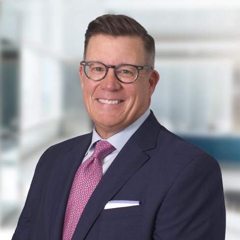 Man in a navy suit, glasses, and red patterned tie, smiling in a modern, brightly lit corporate law office—ideal for those seeking experienced lawyers in Chicago.