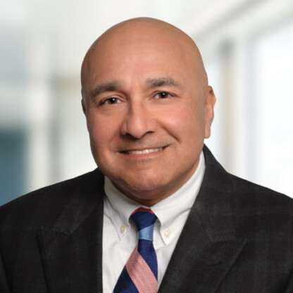 A bald man in a suit, white shirt, and striped tie smiles at the camera in a brightly lit corporate law office, reflecting the professionalism of lawyers in Chicago.