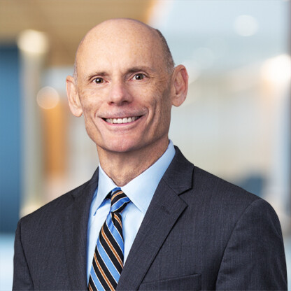 Bald man in a dark suit, blue shirt, and striped tie smiling in a modern, blurred office setting—an image that captures the professionalism often seen at top Chicago law offices.