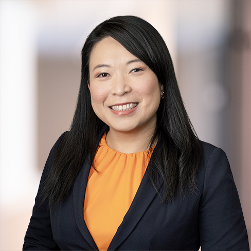 Woman with long black hair wearing an orange blouse and dark blazer, smiling, posed against a blurred indoor background—perfect for representing lawyers in Chicago or a modern corporate law office.