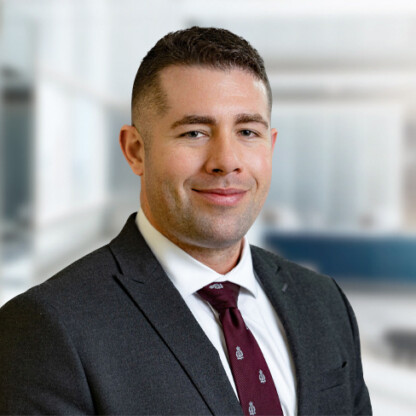 A man in a dark suit, white shirt, and red tie smiles at the camera in a modern, blurred office setting, reflecting the professionalism found in top Chicago lawyers and law offices.