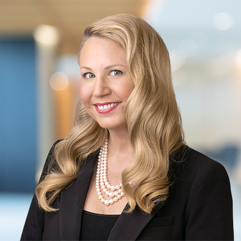 A woman with long blonde hair, wearing a black blazer, a black top, and a layered pearl necklace, smiles in a professional indoor setting—reflecting the polished confidence often seen among Chicago lawyers and those specializing in intellectual property law.