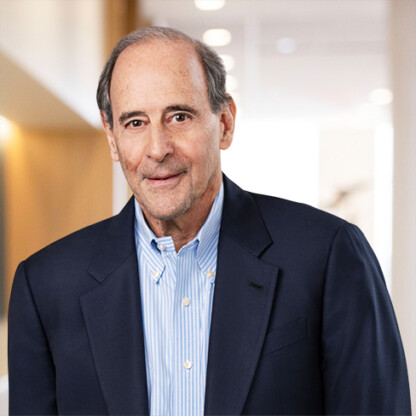 An older man with short gray hair wearing a navy blazer and blue striped shirt stands in a brightly lit hallway of a corporate law office with leading Chicago lawyers.