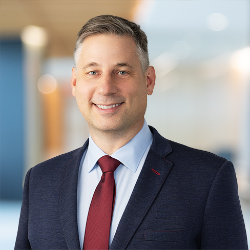 A man in a navy suit and red tie smiles at the camera in a modern, brightly lit corporate law office, reflecting the professional atmosphere of lawyers in Chicago.