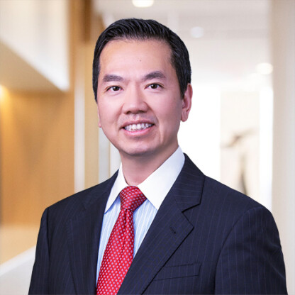 A man in a dark pinstripe suit with a red tie stands in a brightly lit, modern corporate law office hallway, smiling at the camera.