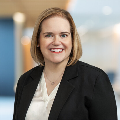 Smiling woman with short blonde hair wearing a black blazer and white blouse, standing in a modern corporate law office, representing Chicago lawyers.
