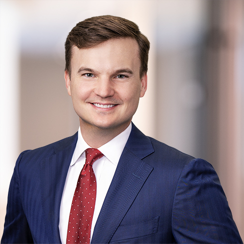 Man in a blue suit and red tie smiling, standing in front of a blurred indoor background at a corporate law office, ready to provide litigation support.