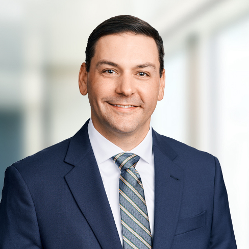 A man in a blue suit, white shirt, and striped tie smiles at the camera, standing in a brightly lit law office—a welcoming professional among Chicago lawyers.