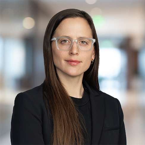 A woman with long brown hair and glasses wearing a black blazer stands in front of a blurred corporate law office, representing the professionalism of Chicago lawyers.