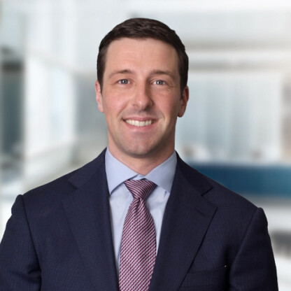 A man in a suit and tie smiles while standing in a modern, light-filled corporate law office.