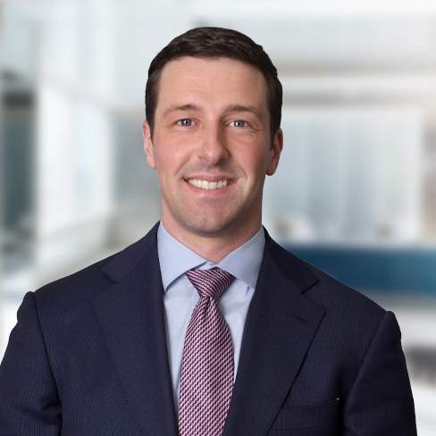 A man in a suit and tie smiles while standing in a modern, light-filled corporate law office.