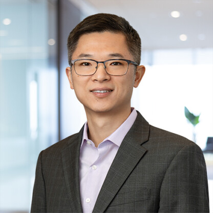 A man wearing glasses and a gray suit jacket over a light purple shirt stands in a modern office setting, representing lawyers in Chicago.